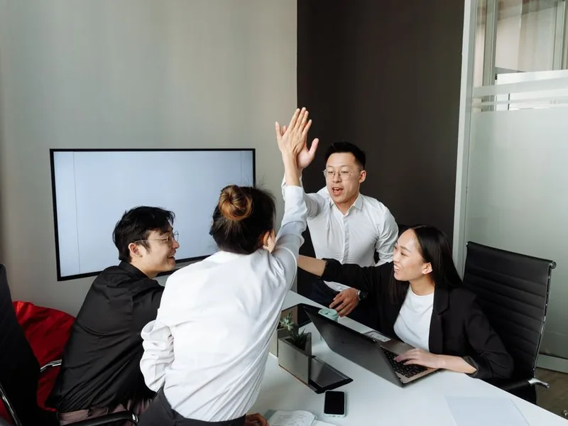 A group of Asian colleagues high-fiving in an office during a business meeting, showcasing teamwork and success.