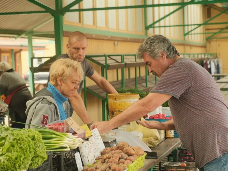 A farmer's market scene with vendors selling fresh produce including greens and potatoes.