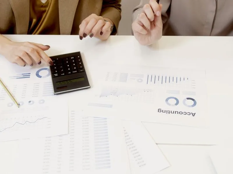 Two professionals analyzing financial documents with a calculator.
