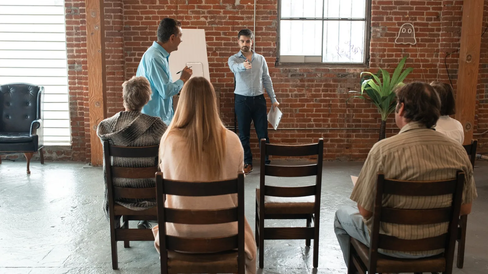 A group of adults attending an indoor workshop with a brick-wall backdrop.