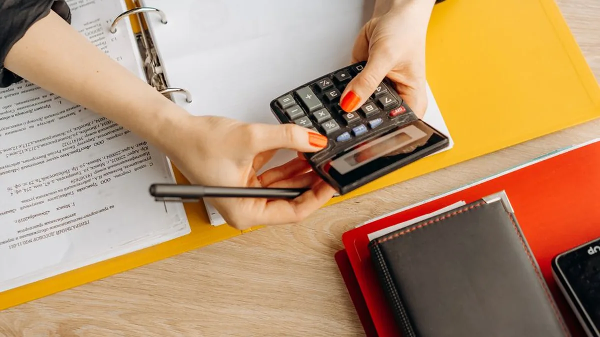 Hands using a calculator at a desk with documents and folders, ideal for finance or accounting themes.